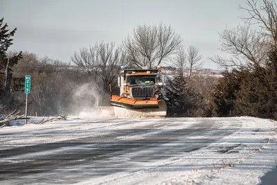 A snowplow clears a rural road in winter, showcasing winter maintenance.