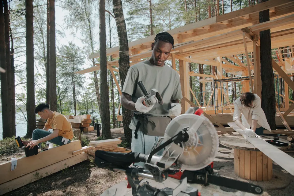 Construction crew building a wooden structure outdoors in a forest setting.