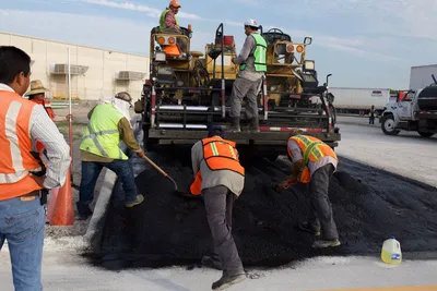 Construction workers laying asphalt on a road with heavy machinery.